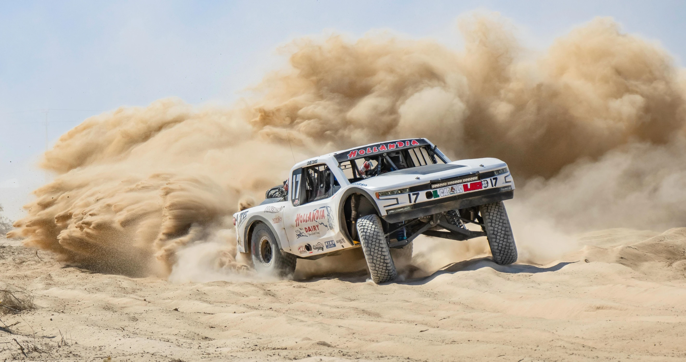 a truck kicking up sand on top of a sandy field