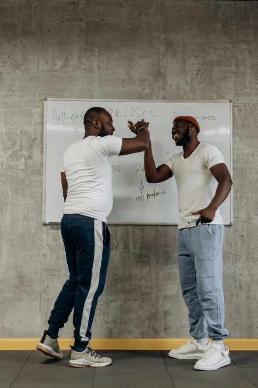 two men at a white board pointing with both hands