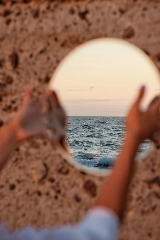 someone holding their hands in front of a mirror near the ocean