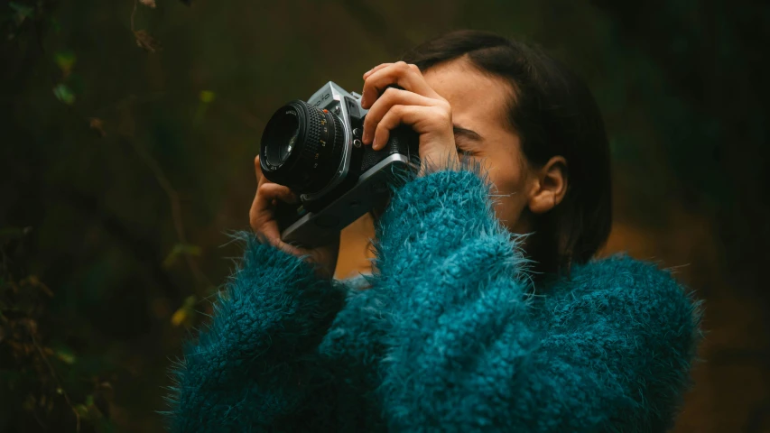 a woman wearing a blue sweater holding a camera