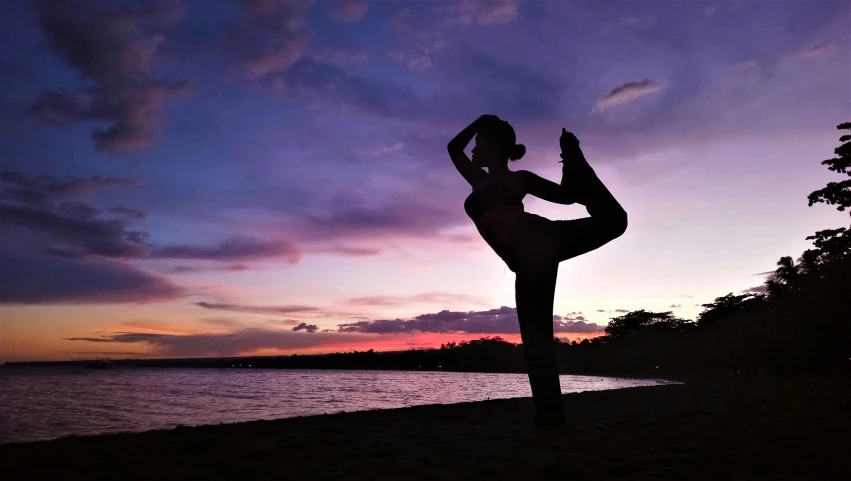 a woman doing yoga outside on a beach at sunset