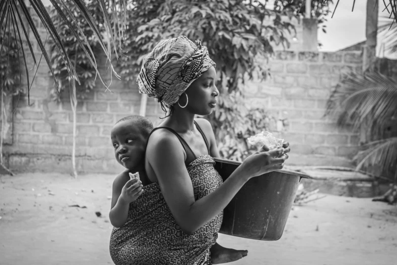 a woman holds her child outside with a bucket