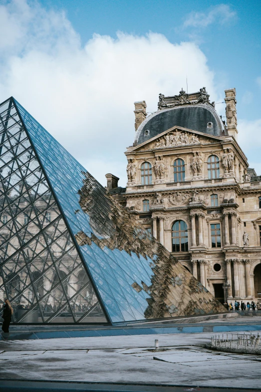 people are walking past the glass pyramid and a building