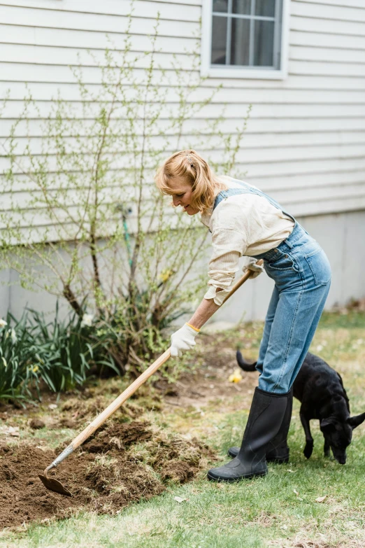 woman holding a wooden stick digging the ground with her dog nearby