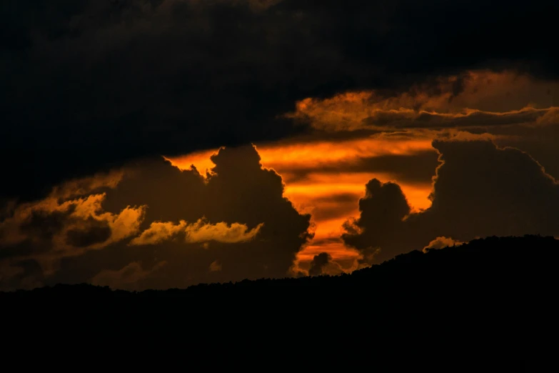 a cloud is silhouetted as it moves across a dark sky