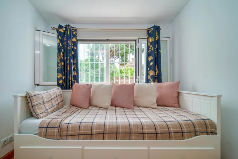a window with blue curtains, plaid bedding, and red pillows
