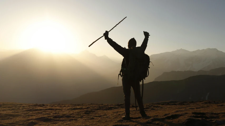 the silhouette of a person with a large backpack holding two sticks