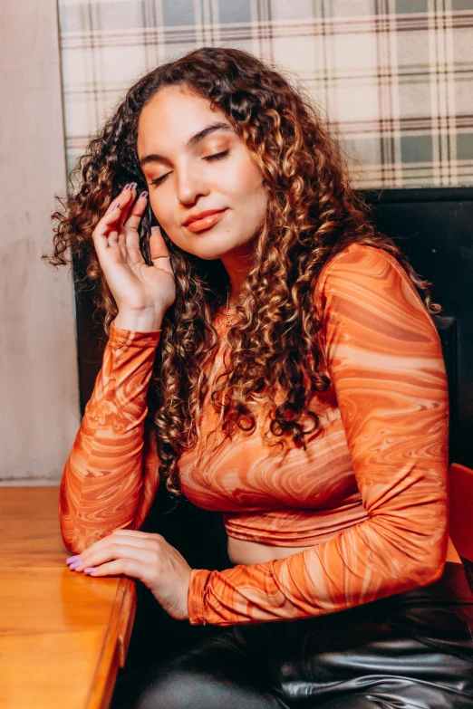 woman in orange shirt and black pants talking on cell phone