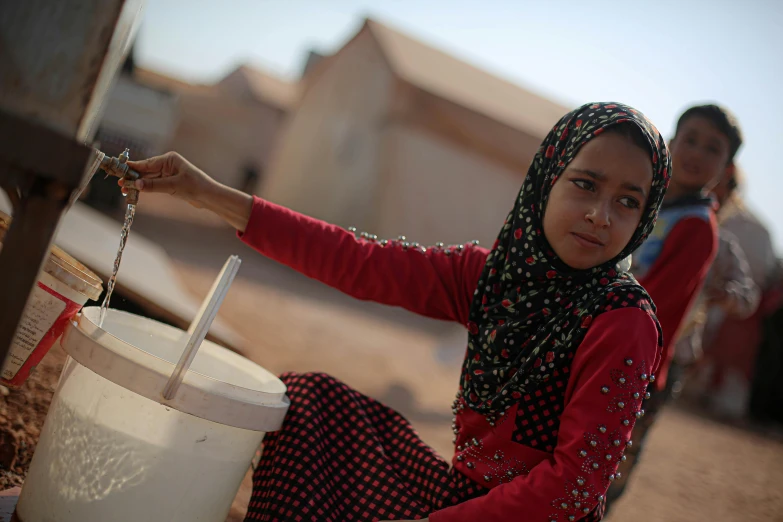 a woman in a head scarf is holding soing by a bucket