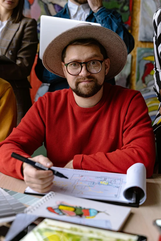 man wearing hat and glasses sitting at a table with paper