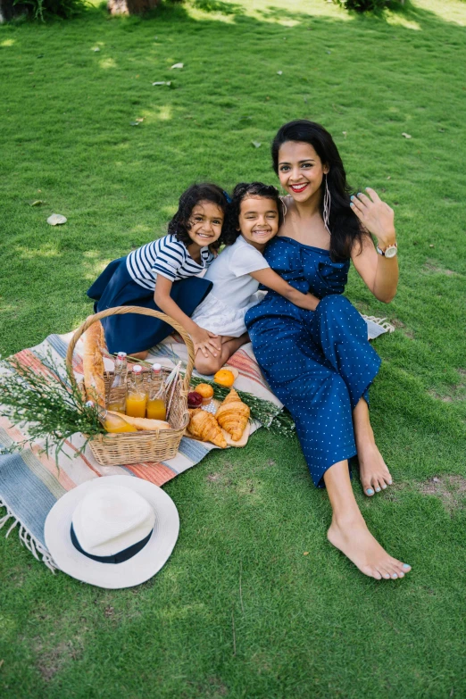 three children sitting on a blanket in the grass near a picnic basket