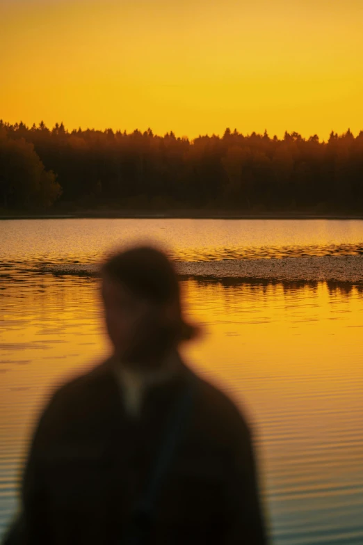 a guy walking on the beach by a sunset with trees behind him