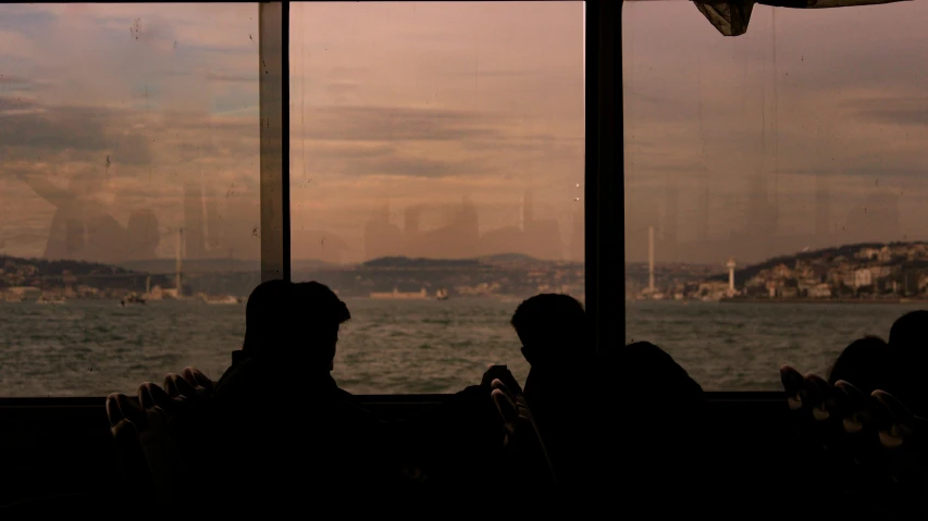 silhouettes of people looking out a window with a view of the water