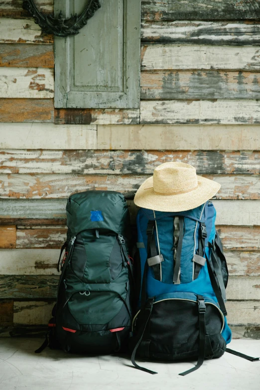 two backpacks are stacked next to each other with a hat on the top of one