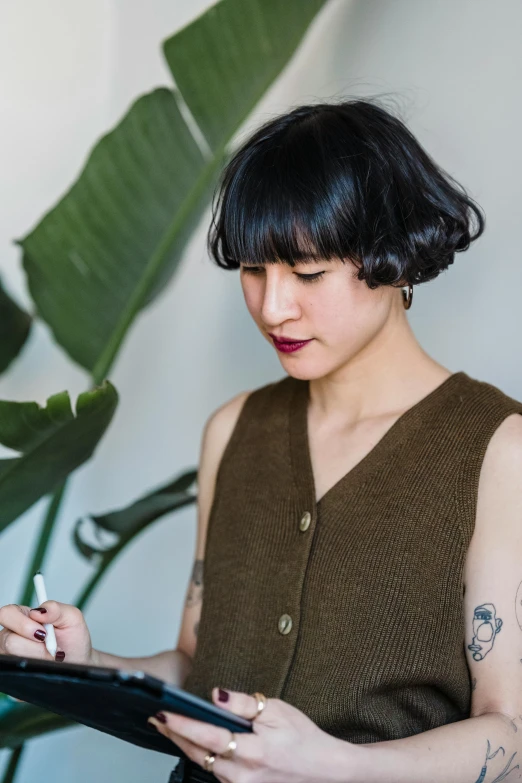 woman with tattoo holding tablet standing in front of plant