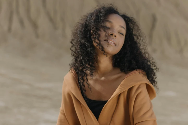 a woman in an orange jacket standing in front of sand and hills