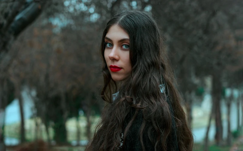 a woman with long brown hair standing in the woods