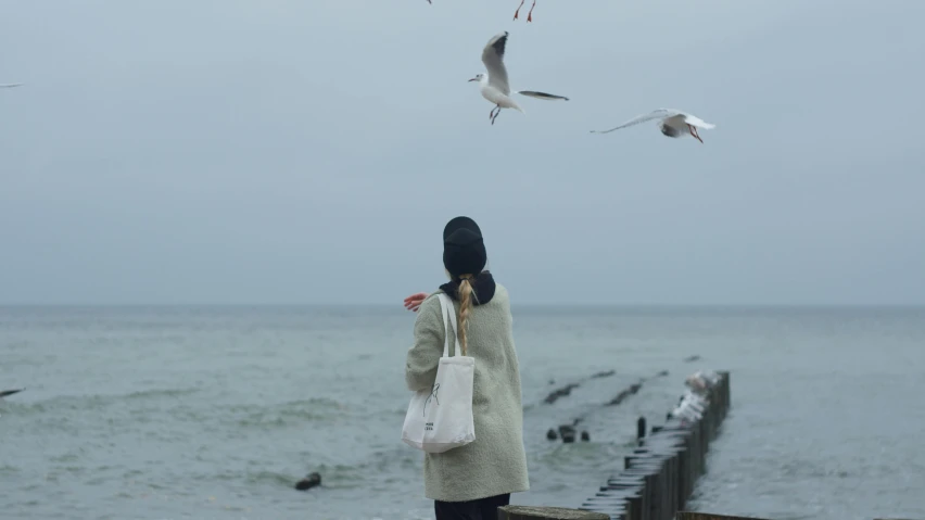 a woman standing at the end of a wooden pier holding a shopping bag