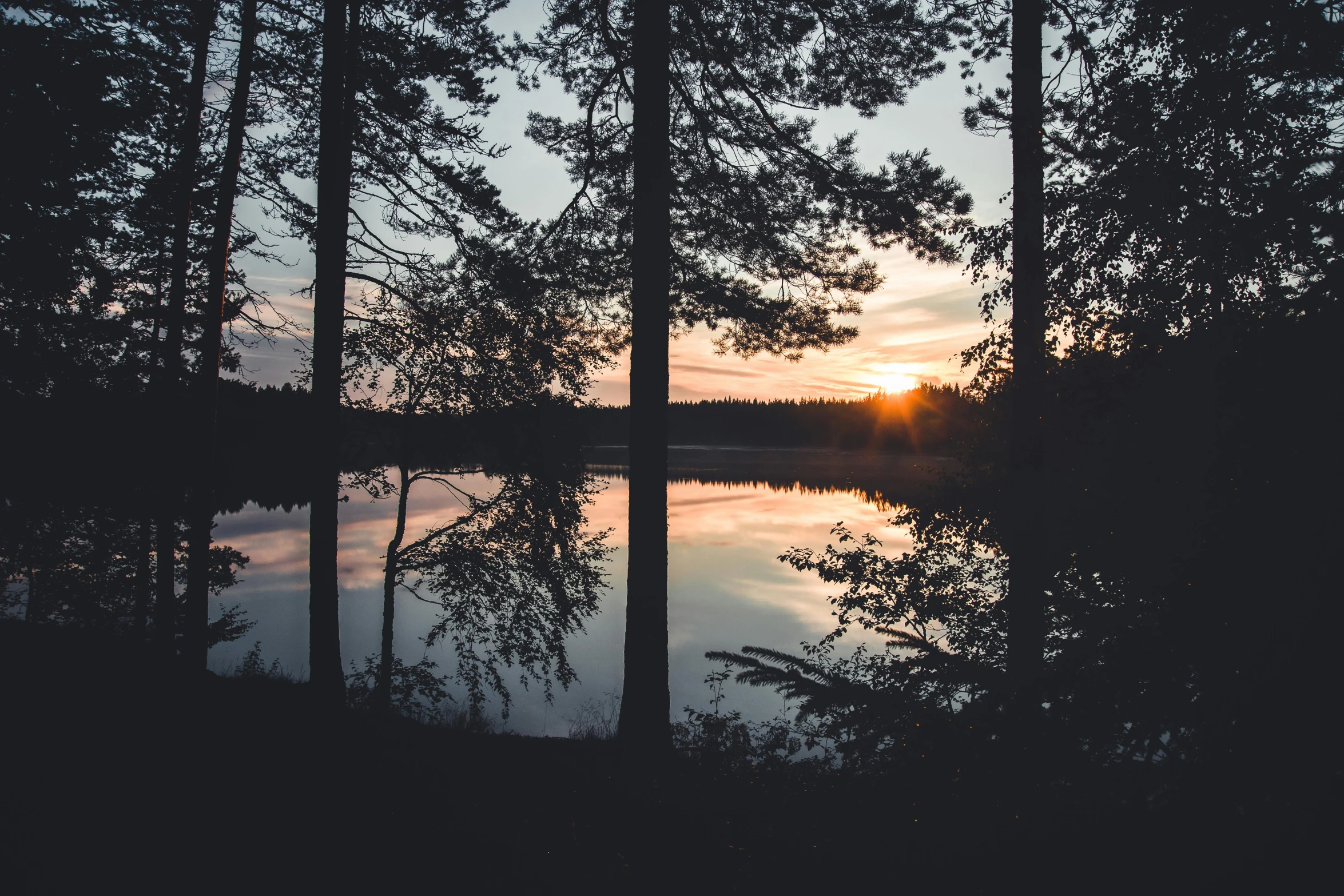 a sunset reflects in the calm water of a lake