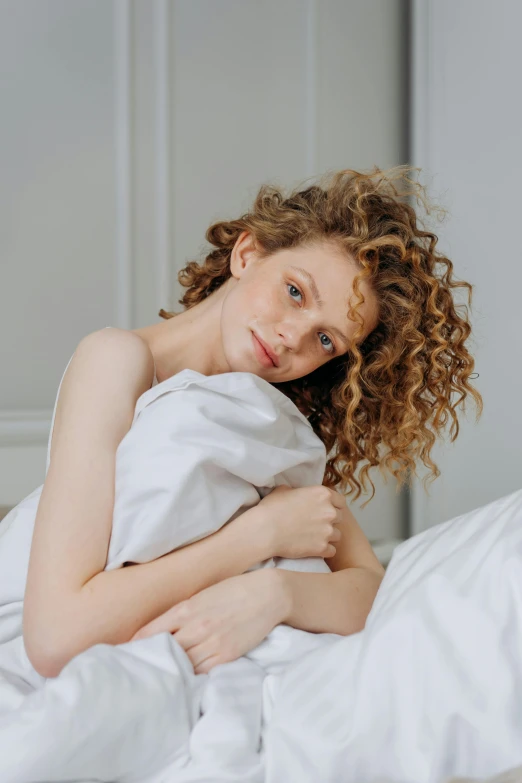 a beautiful young woman laying in bed wrapped in white sheets