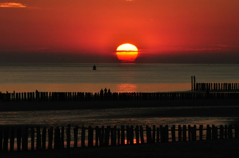 the sun is setting over the ocean with a sailboat in the distance