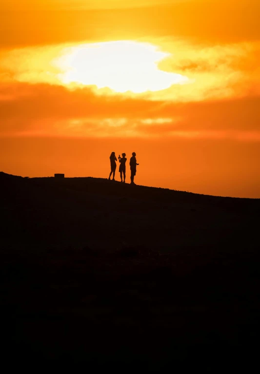 three people on top of a hill at sunset