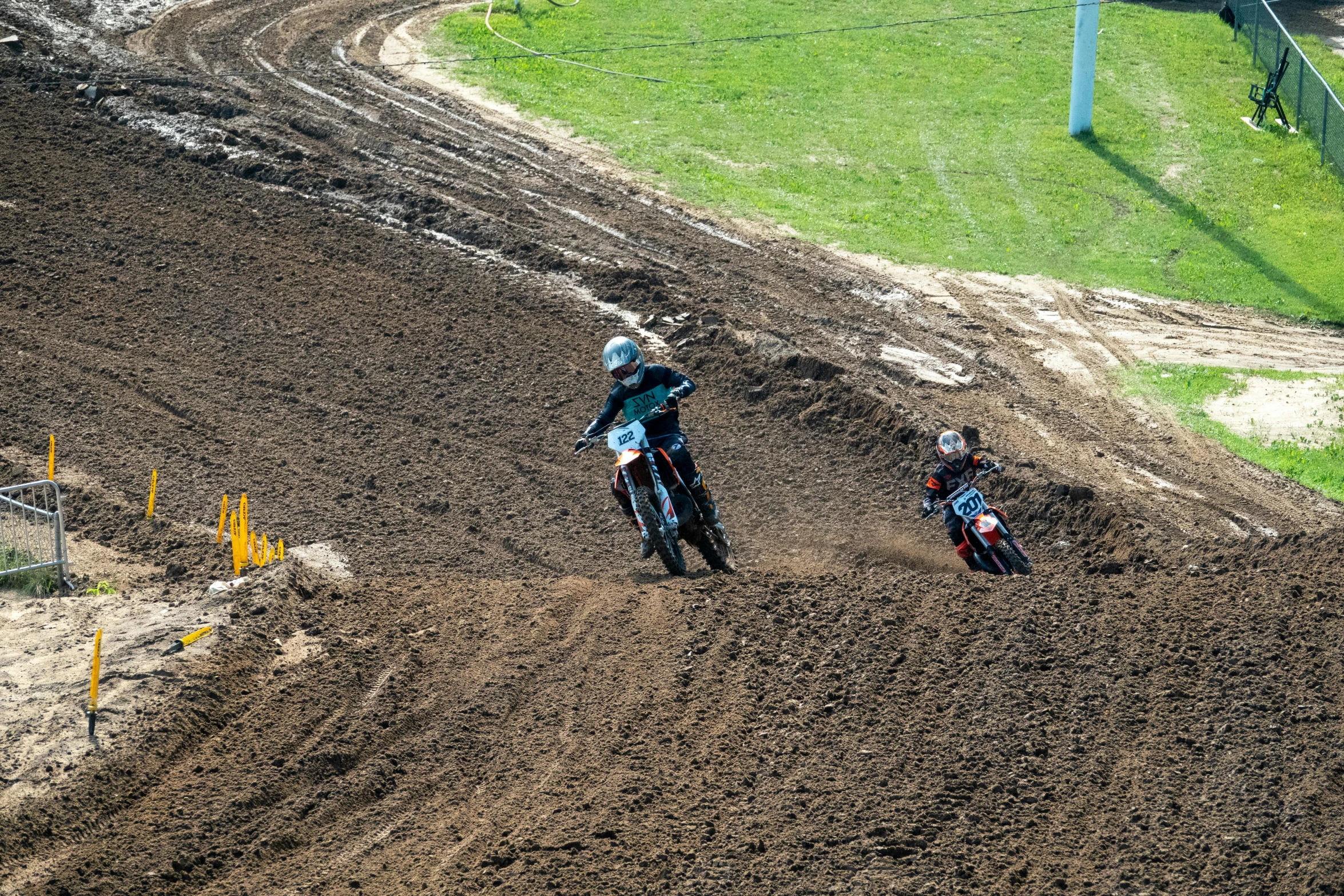 three motorcyclist race on a dirt track near a soccer goal