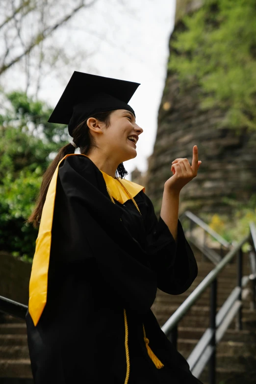 an asian woman in a graduation gown applauding the graduate