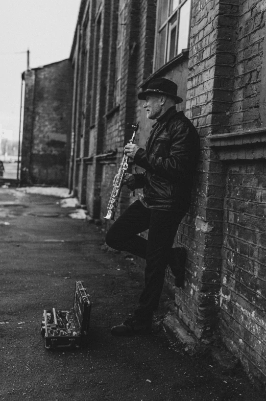 an old man leaning against the wall and playing a saxophone