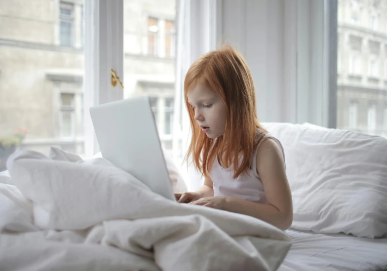 a  sitting on a bed using her laptop
