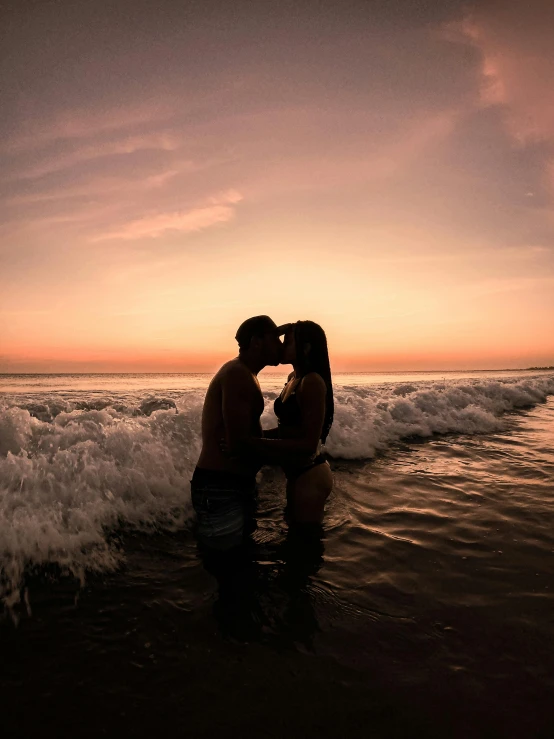 couple kissing on the beach with water crashing into shore