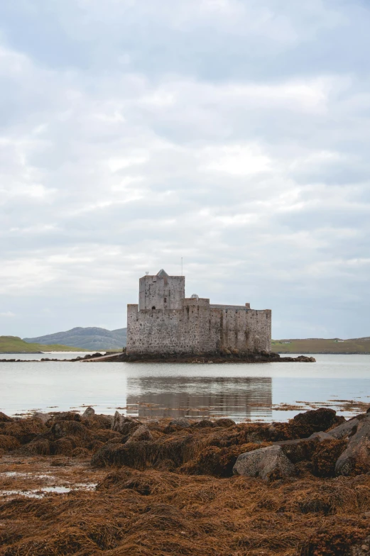 a lonely white castle in the middle of water with large stones around