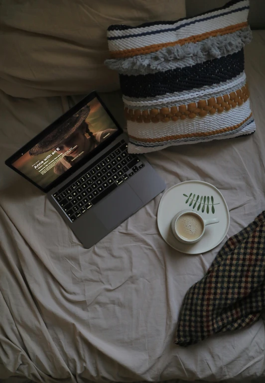 a laptop computer sits on a bed near a cup and saucer