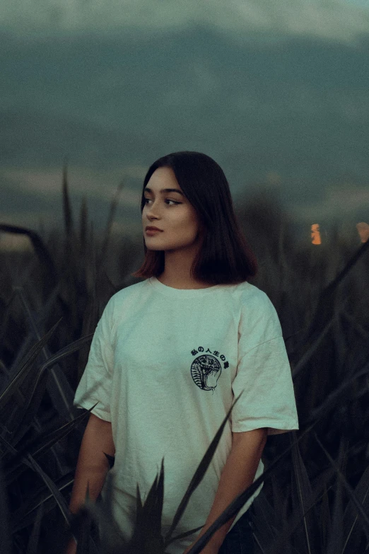 an asian girl in front of tall grasses looks into the distance with a hazy sky behind her