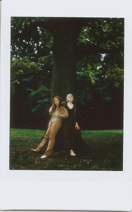 two girls in vintage clothing sitting near a tree