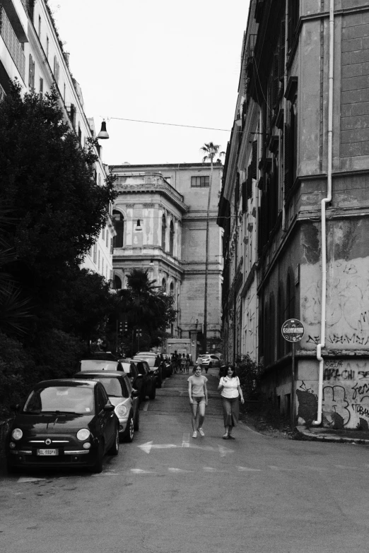 two people walking in the road next to parked cars