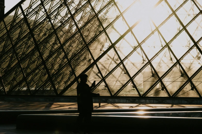 a shadow of a person walking near an artisticly designed glass and steel structure