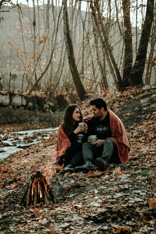 a couple sits together on the ground by a stream