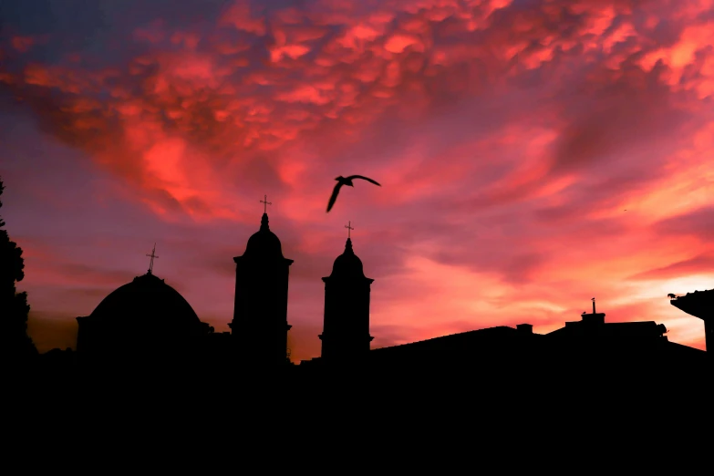 a bird flying over some buildings under a red sky