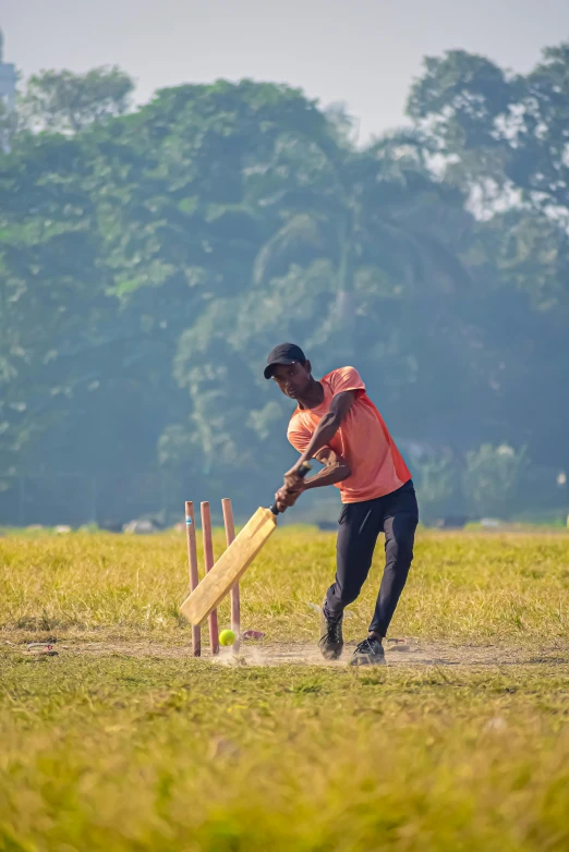 a young man in an orange shirt is holding a wooden cricket bat