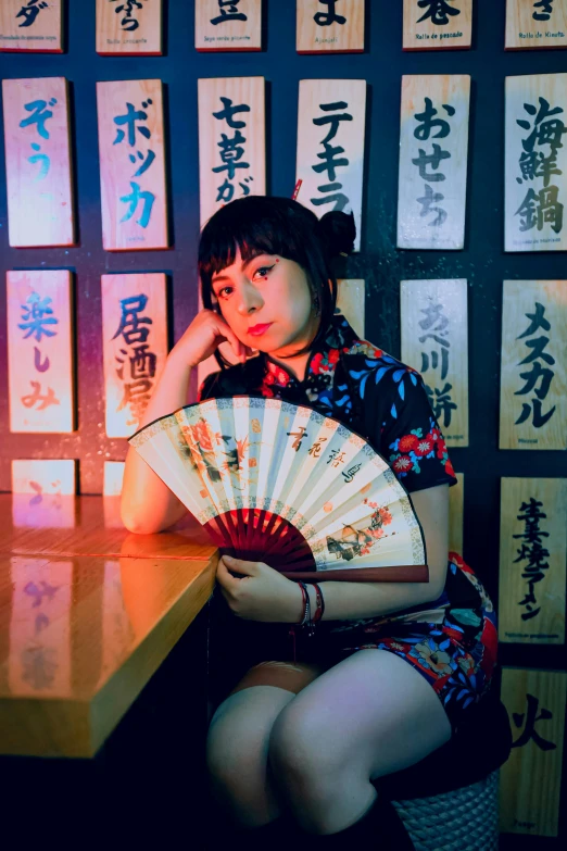 a young woman sits at a table with an oriental fan