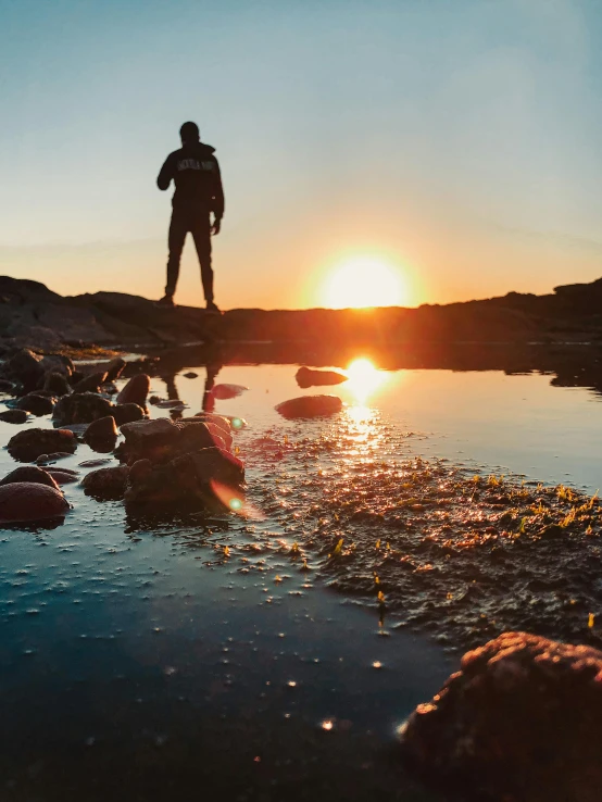 man standing on shore watching the sun set