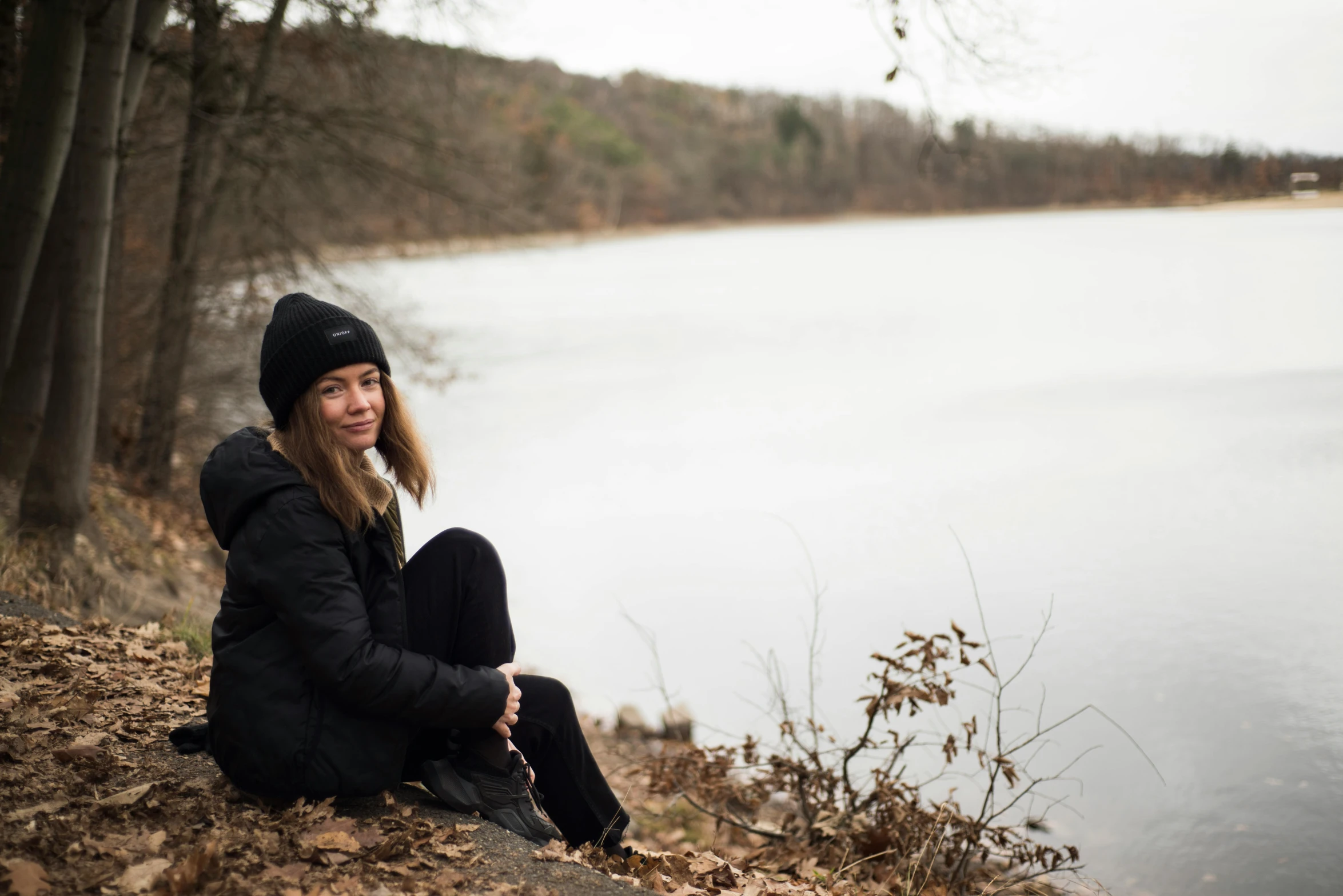 woman sitting near water on the edge of forest