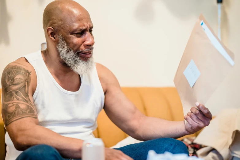 a bald man sitting on the couch holding a sheet of paper with writing