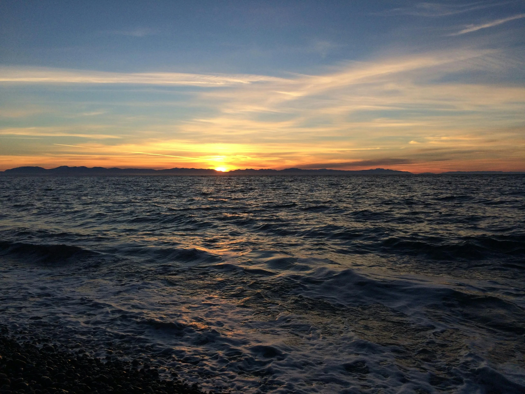 the sun rises over an ocean near the shore