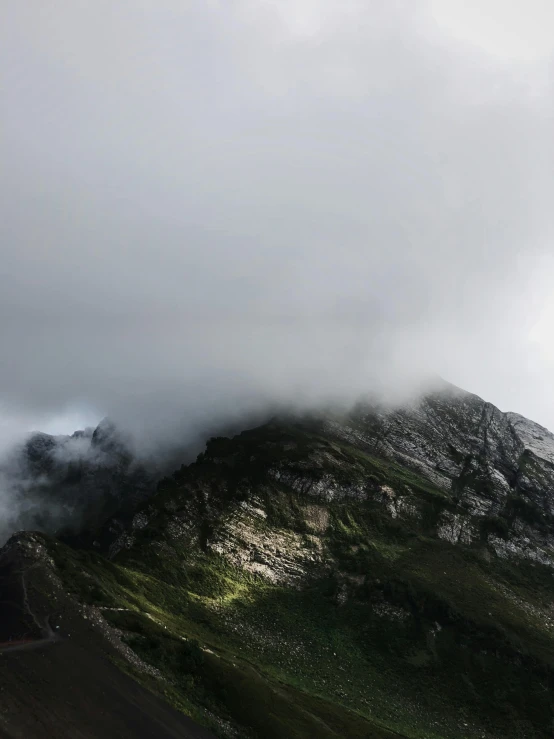 a road going past a mountain with clouds coming from it