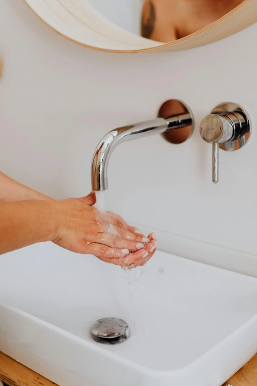 person washing hands under a bathroom mirror in bathroom