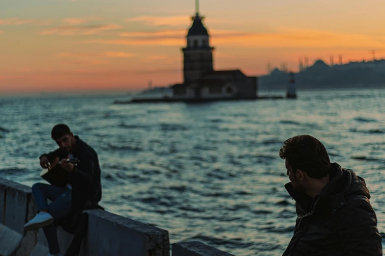 two men sit on the waterfront as the sun sets