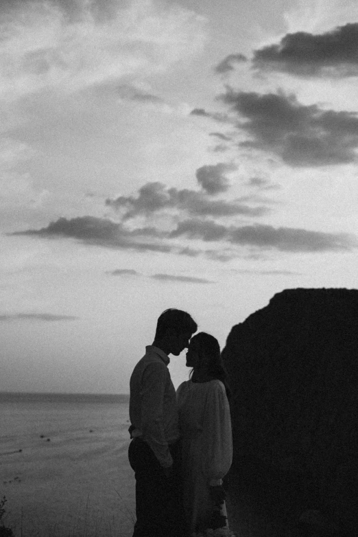 black and white pograph of a couple hugging each other by the beach at sunset