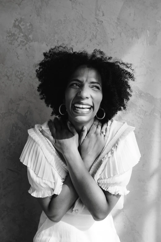 a woman with curly hair laughing and holding her hands together